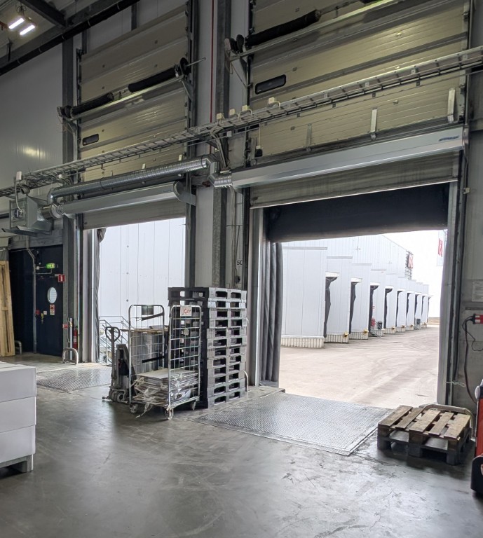 Två öppna industriportar med luftridåer monterade ovanför som fungerar som en osynlig dörr som hindrar den kylda luften från att åka ut genom öppningarna